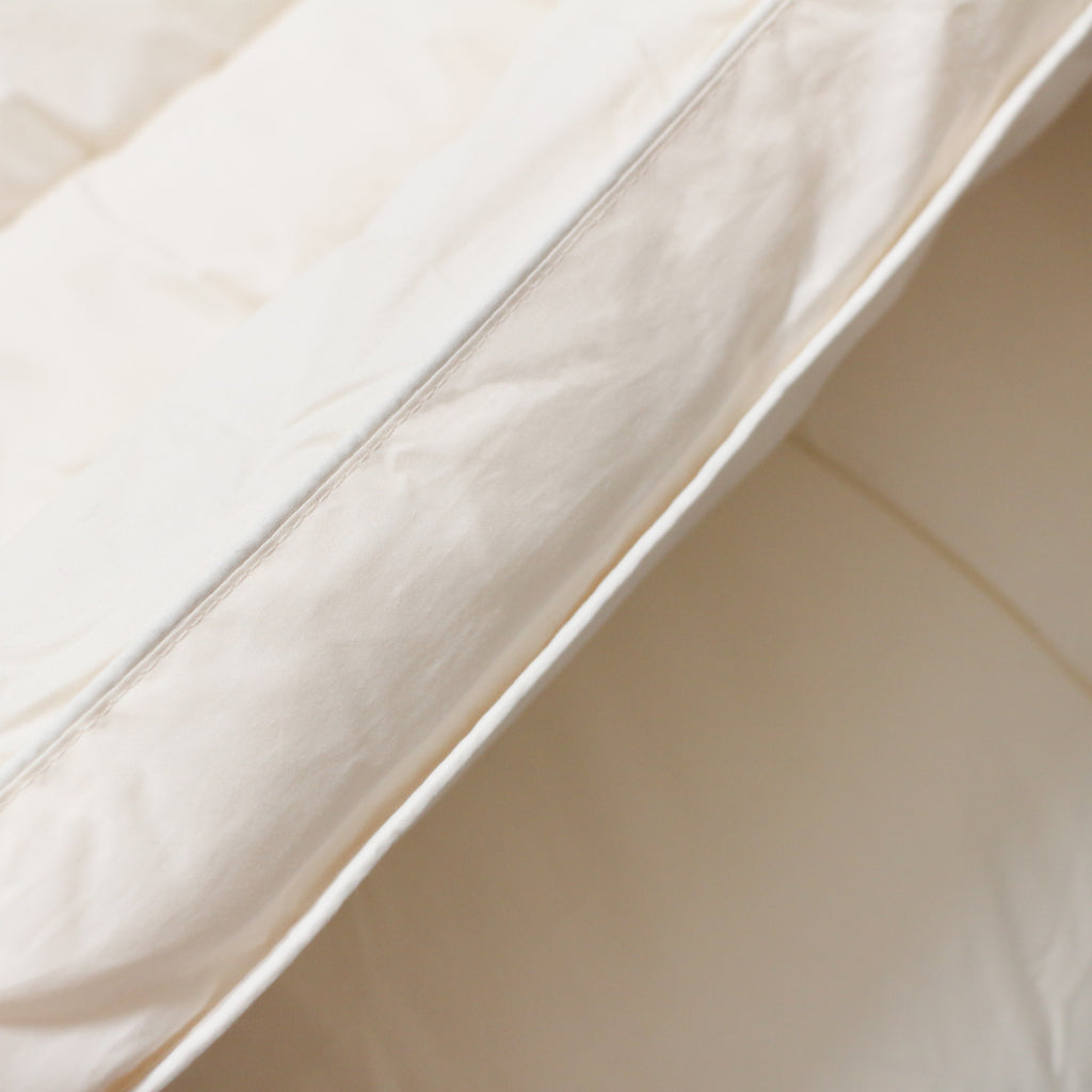 Close-up edge detail of Purevana wool mattress topper — natural cotton percale shell with merino wool fill